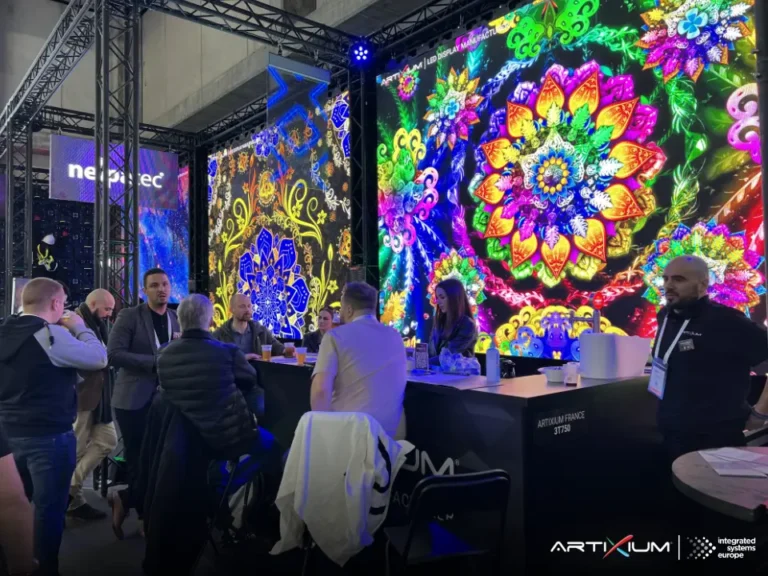 Visiteurs réunis autour du bar du stand devant un mur d'images LED aux motifs floraux colorés