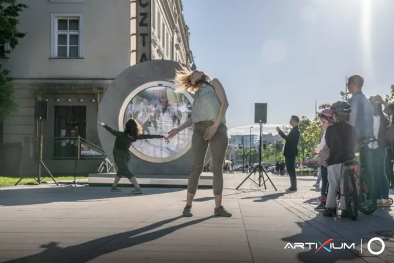Deux danseuses évoluent devant le portail circulaire à écran LED, sous le regard des passants
