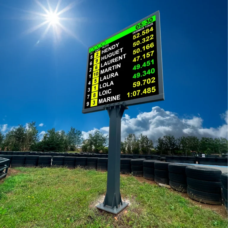Pole-mounted LED screen showing kart standings and lap times beside a tyre-lined karting circuit