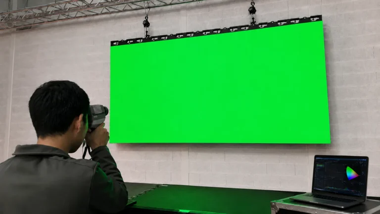 Technicien mesure un mur LED affichant une mire verte, logiciel de calibration sur l'ordinateur
