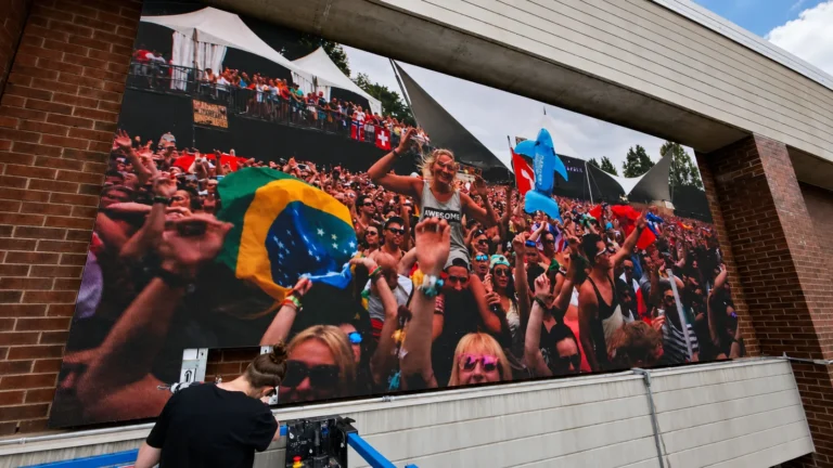 Façade LED display showing a festival crowd, with a technician on a lift at the foot of the wall