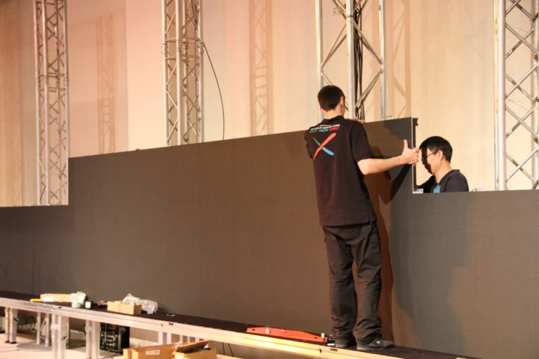 LED video wall being assembled on stage, two technicians aligning cabinets between truss towers