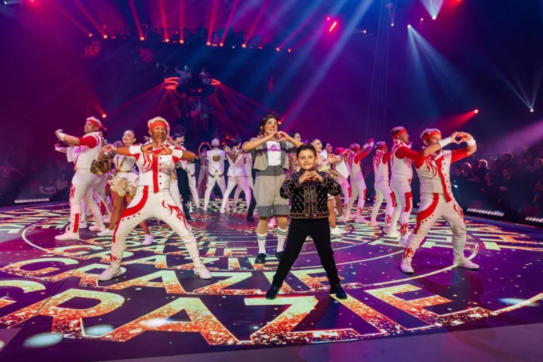 Sol LED – Artistes sur la piste LED du cirque affichant le mot GRAZIE, projecteurs et public en fond