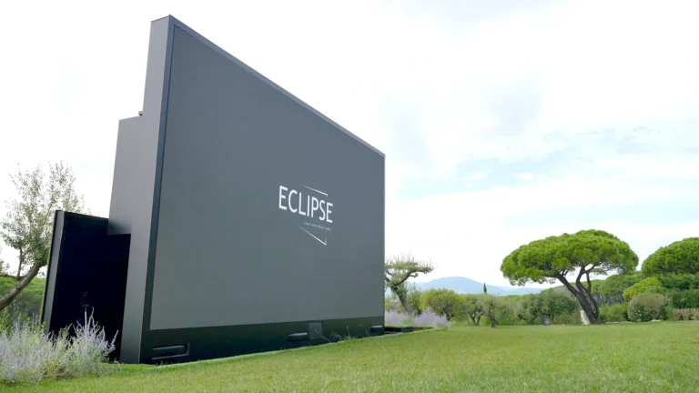 LED screen terrace – ECLIPSE outdoor LED screen seen from behind in a Mediterranean garden, parasol pines around