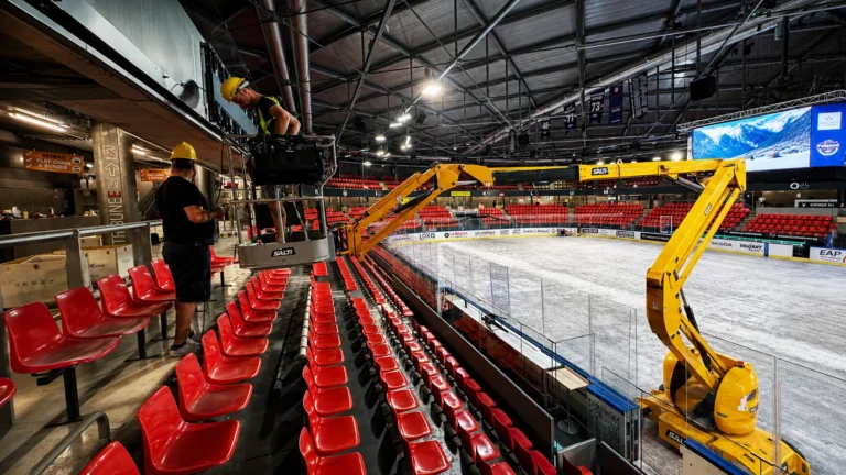 LED cabinets being installed from an articulated boom lift above the stands of an ice rink