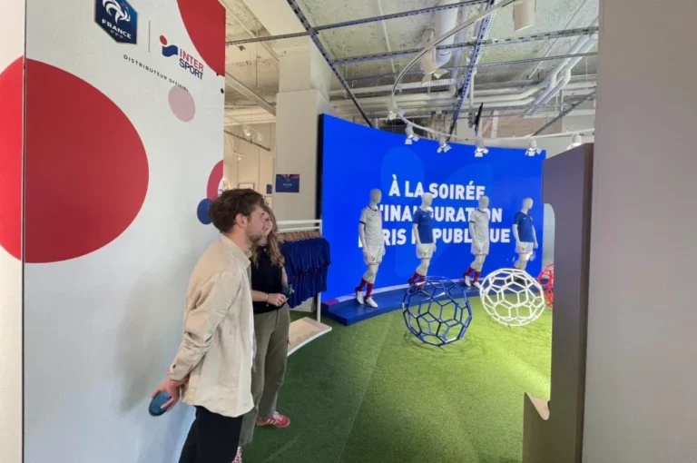 Écran LED magasin Intersport – Mur d’images LED incurvé bleu derrière les mannequins en maillot, visiteurs sur la pelouse synthétique