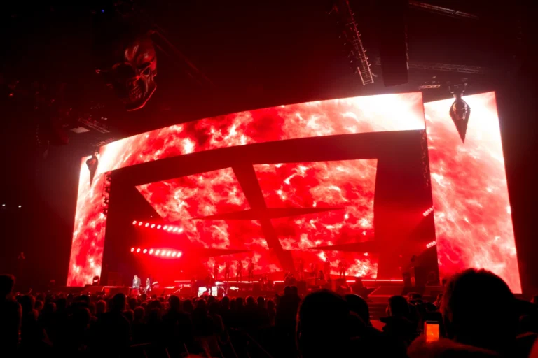 Giant LED video wall of red flames framing the stage, packed arena in front of it