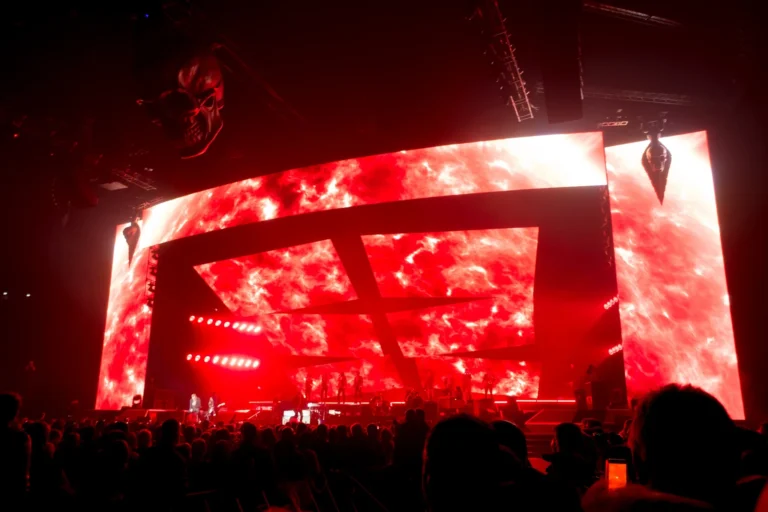 Huge curved LED video wall glowing red above the stage, audience silhouetted in the foreground