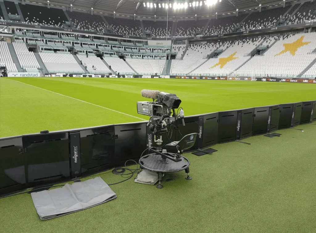 Pitch-side perimeter LED system from behind, a TV camera on its dolly in the empty stadium
