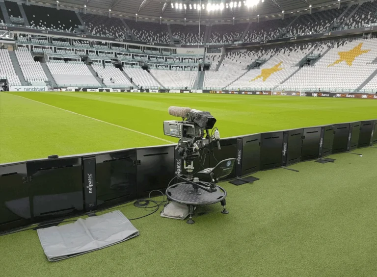Pitch-side perimeter LED system from behind, a TV camera on its dolly in the empty stadium
