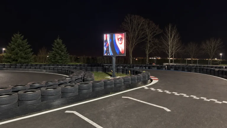 Écran LED COBALT sur mât en bordure de piste de karting, visuel coloré dans la nuit