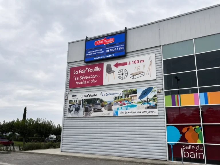 Vue d’ensemble de la façade, écran LED bleu annonçant les horaires au-dessus des bâches publicitaires