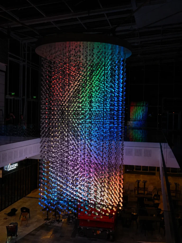 Cylinder of LED spheres showing a rainbow gradient across the shopping centre atrium