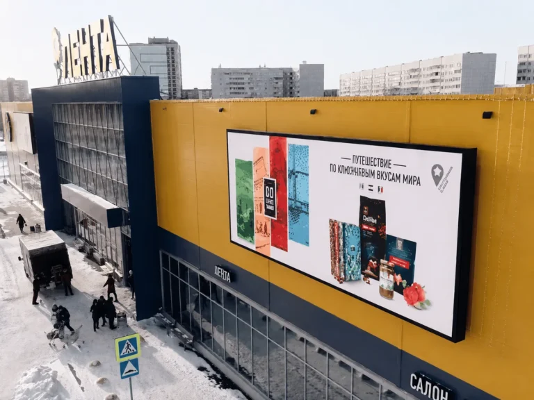 Wide LED screen seen at an angle on the store’s yellow facade, snowy apartment blocks behind