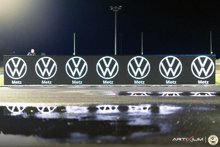 Système LED périmétrique affichant un logo sponsor répété au bord d'une piste mouillée la nuit