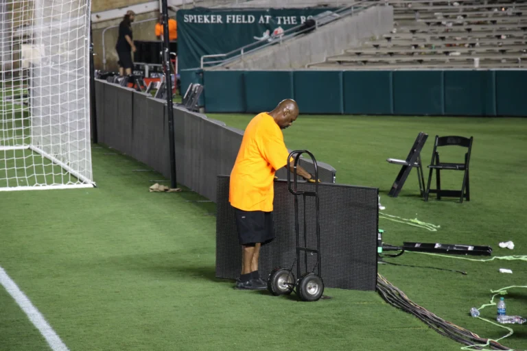 Technician moving a perimeter LED cabinet on a trolley at the edge of the pitch