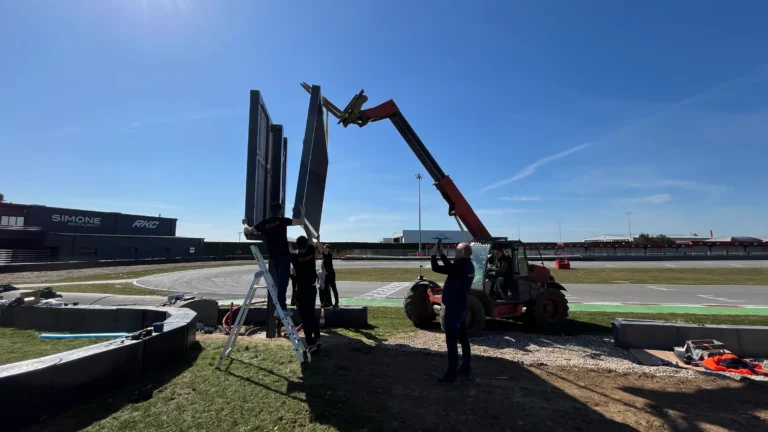 Technicians and a telehandler raising two COBALT LED screens trackside under a clear sky