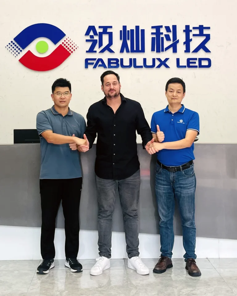 AXLED et Fabulux : trois hommes posent dans le hall d’accueil, devant le logo mural Fabulux LED