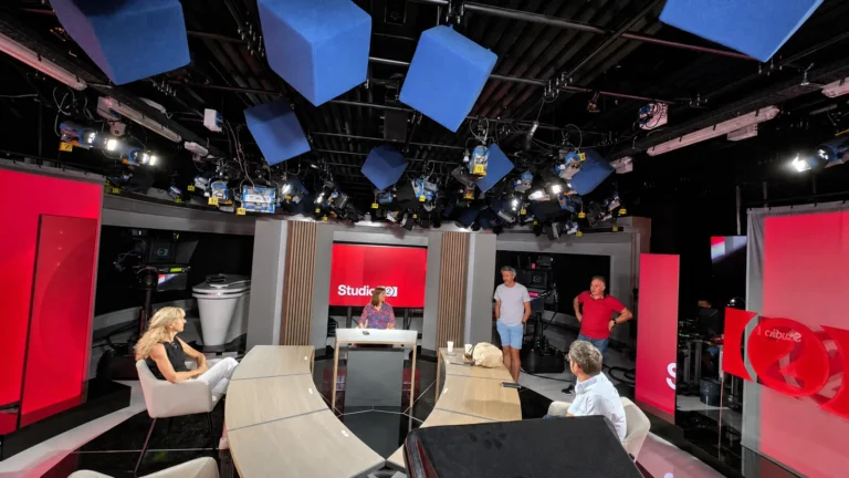 Écran LED studio TV – Plateau TV aux murs d’images LED rouges, grille de projecteurs et invités assis autour du bureau