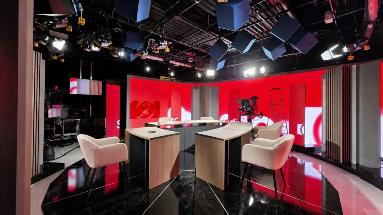 Studio RTL vide, fond LED incurvé rouge aux couleurs de la chaîne, caméra et fauteuils sur sol brillant