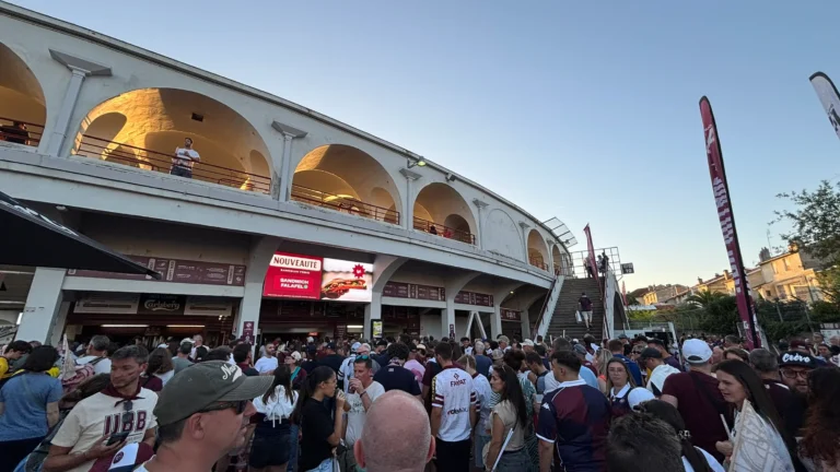 Écran LED publicitaire sous les arcades du stade, foule de supporters à l’entrée en fin de journée