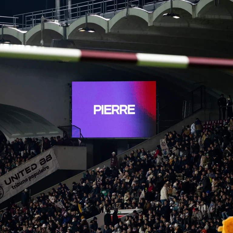 Écran géant LED affichant le prénom d’un joueur au-dessus des tribunes pleines, match en nocturne