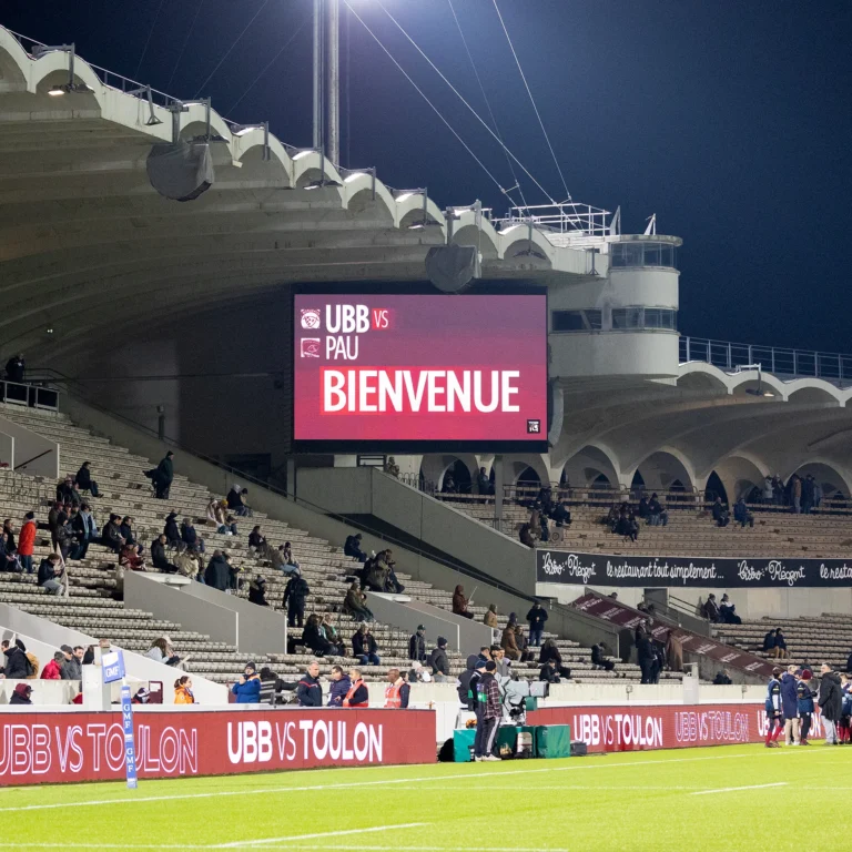 Écran géant LED affichant le message d’accueil du match, tribunes en cours de remplissage