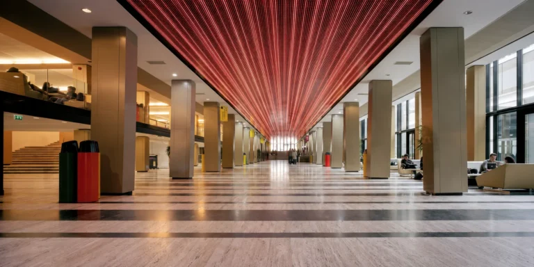 Red LED ceiling receding in perspective over the hall, students seated along the sides