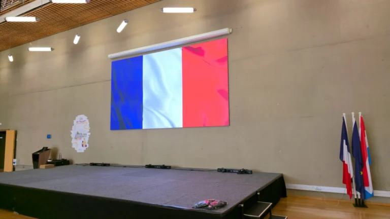 Écran LED lycée – Écran LED QWARTZ mural affichant un drapeau tricolore au-dessus de la scène d’une salle polyvalente