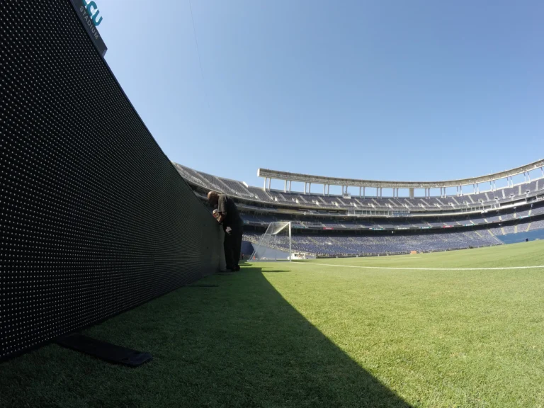 Perimeter LED system running along the edge of the pitch, empty stands under a blue sky