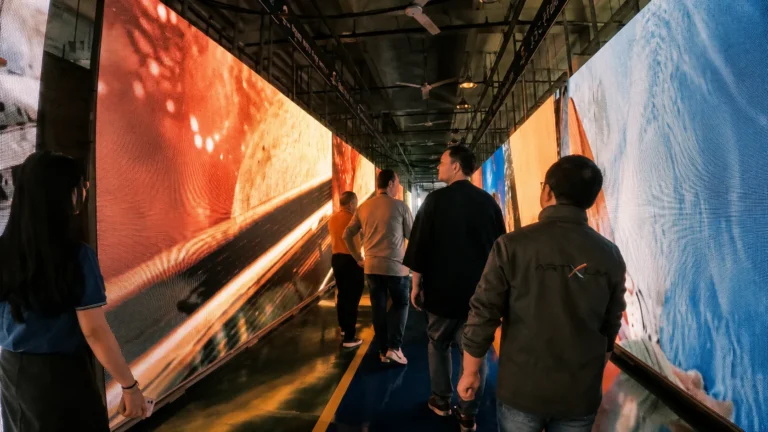 Allée bordée de murs LED allumés dans un hall d'usine, visiteurs de dos
