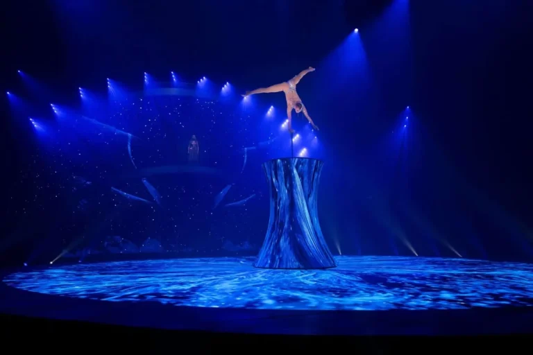 Hand balancer on the LED diabolo with blue visuals, LED floor and starry backdrop