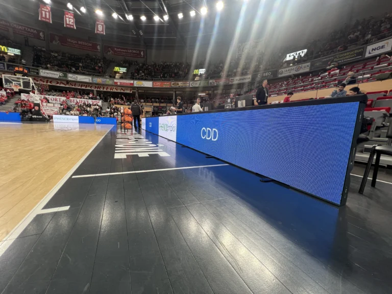 Gros plan sur les dalles LED du système périmétrique bleu bordant le parquet, tribunes en arrière-plan