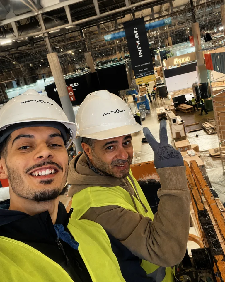 Deux techniciens casqués aux couleurs Artixium pendant le montage d'un stand de salon