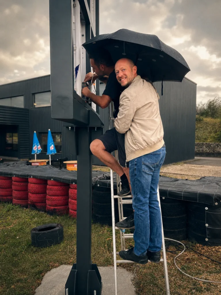 Raccordement d'un écran LED sur mât au bord d'une piste de karting, sous la pluie