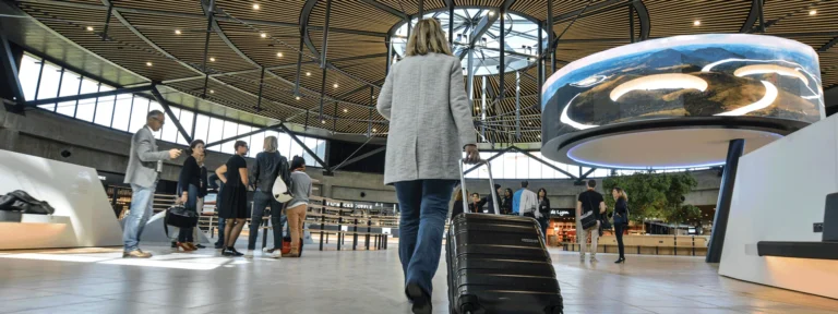 Circular LED screen showing a landscape above the hall, travellers crossing with luggage