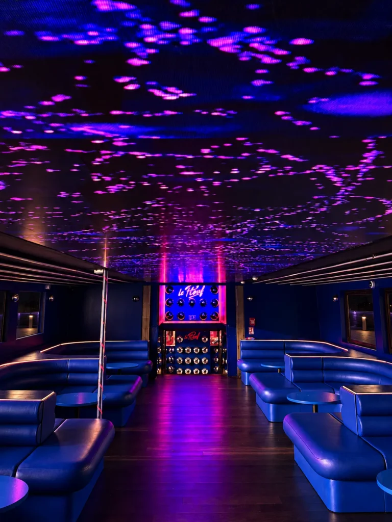 Purple and pink visuals on the LED ceiling of the VIP lounge, blue bench seating